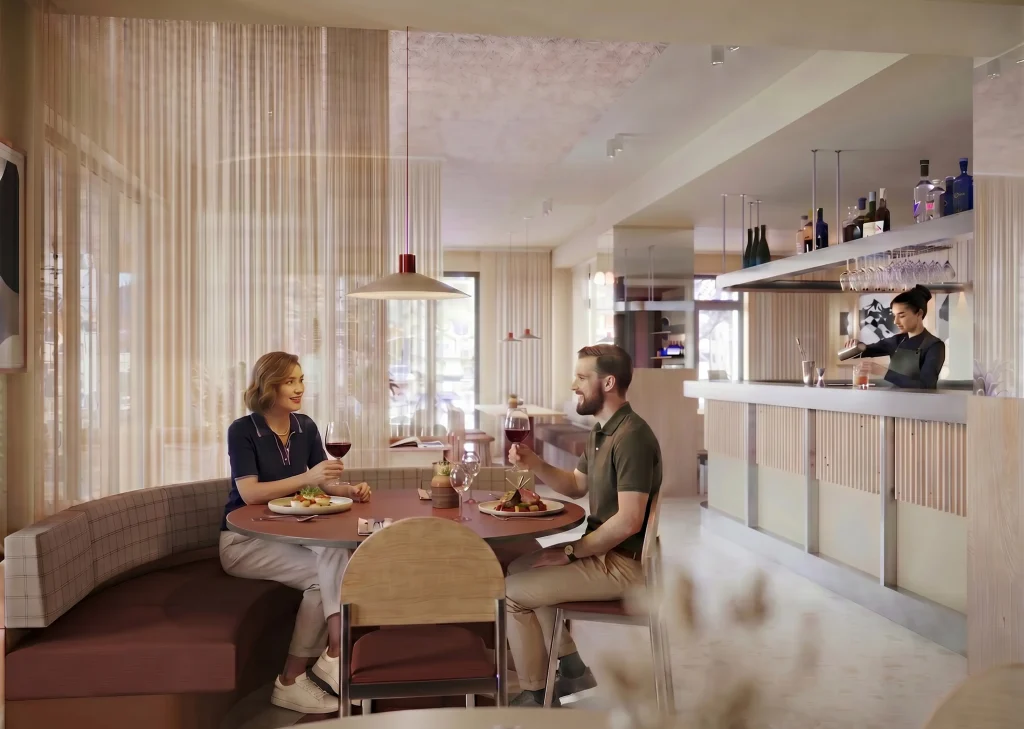 Couple attablé dans un restaurant au design contemporain chaud, dînant avec des verres de vin rouge et des assiettes gastronomiques. La salle est décorée de banquettes à carreaux roses, de rideaux voilés beiges et de suspensions design. En arrière-plan, une barmaid prépare un cocktail derrière le comptoir avec des étagères de bouteilles.